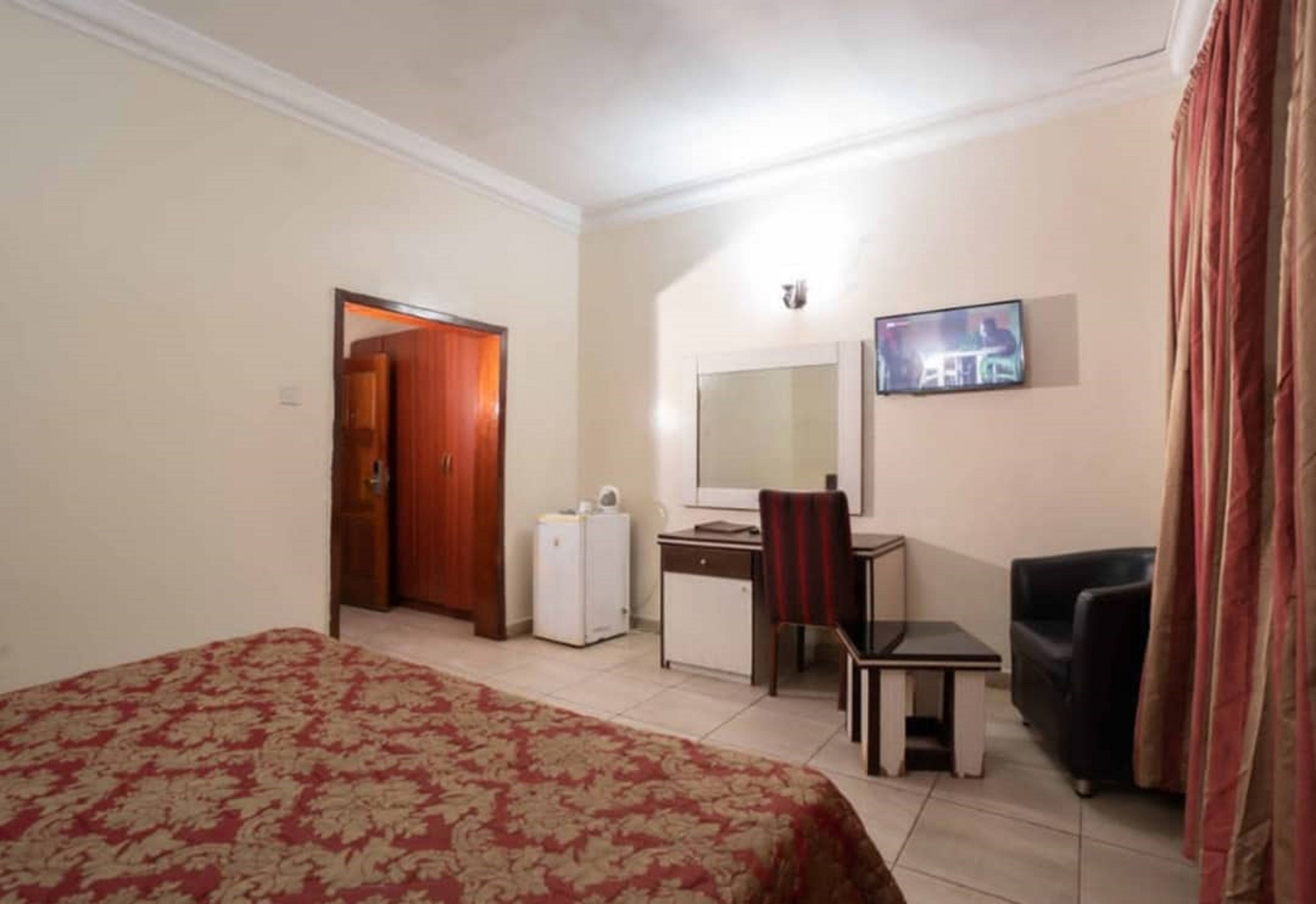 A hotel room with a bed, a desk, a chair, a television, and a wardrobe.
