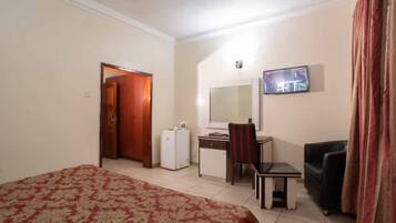 A hotel room with a bed, a desk, a chair, a television, and a wardrobe.