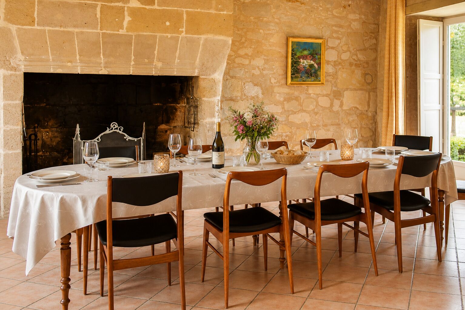 Une salle à manger avec une cheminée en pierre, une table dressée pour six personnes et un tableau accroché au mur.