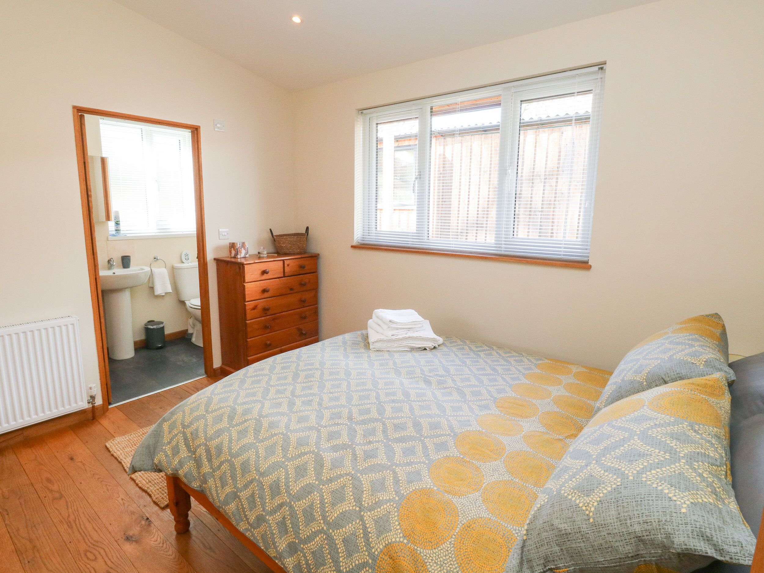 Un dormitorio con cama, cómoda, ventana y baño a la vista a través de una puerta abierta.
