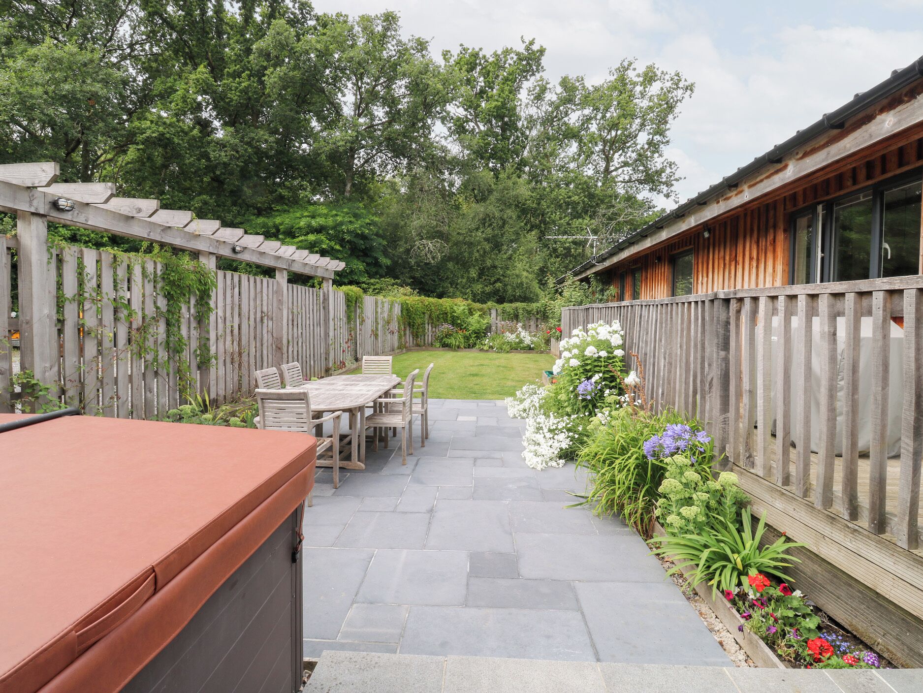 Un espace patio agrémenté d’une pergola en bois, d’une table et de chaises, ainsi que d’un parterre de fleurs.
