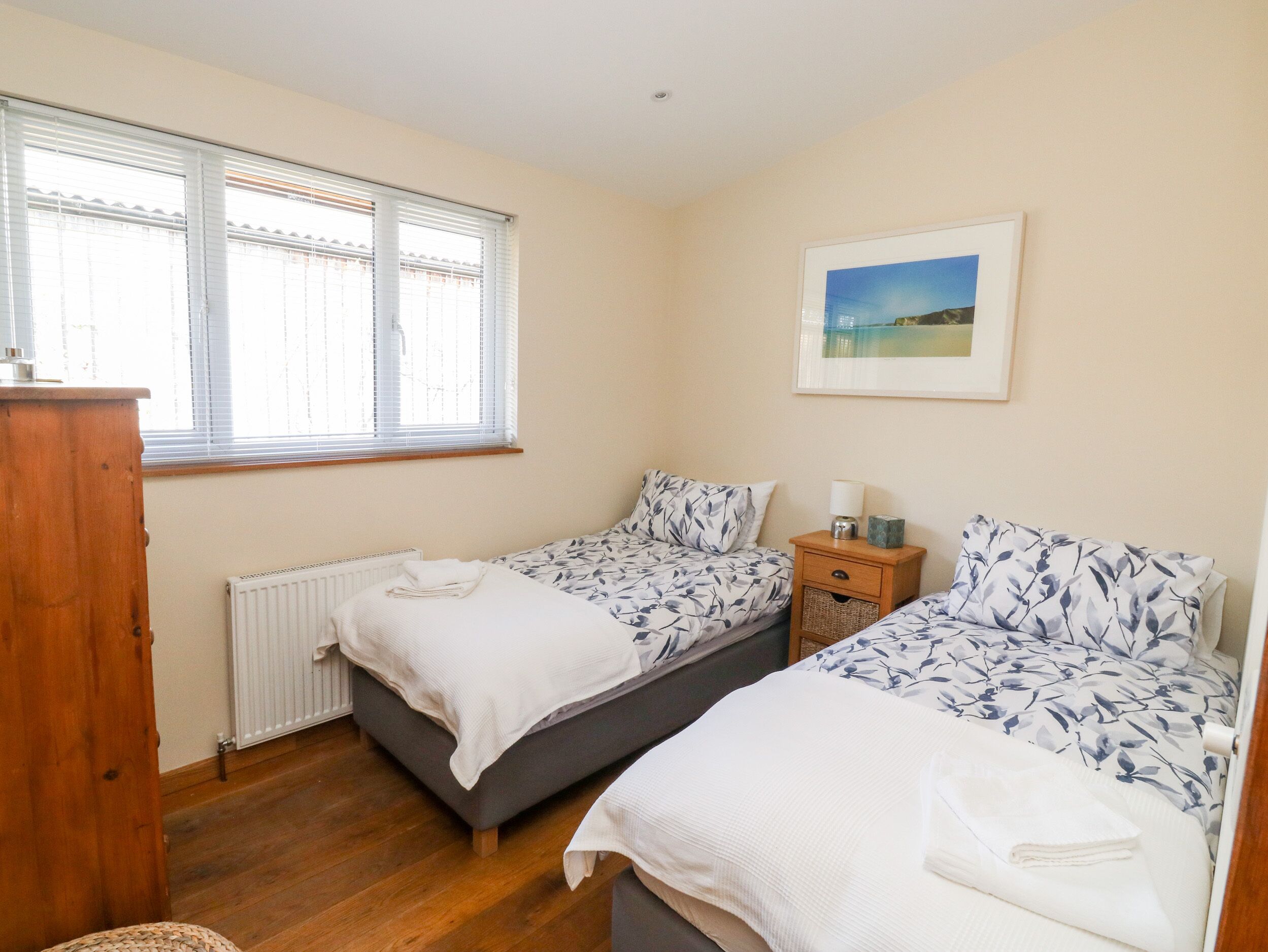 A bedroom with two beds, a radiator, a wooden dresser, and a framed picture on the wall.