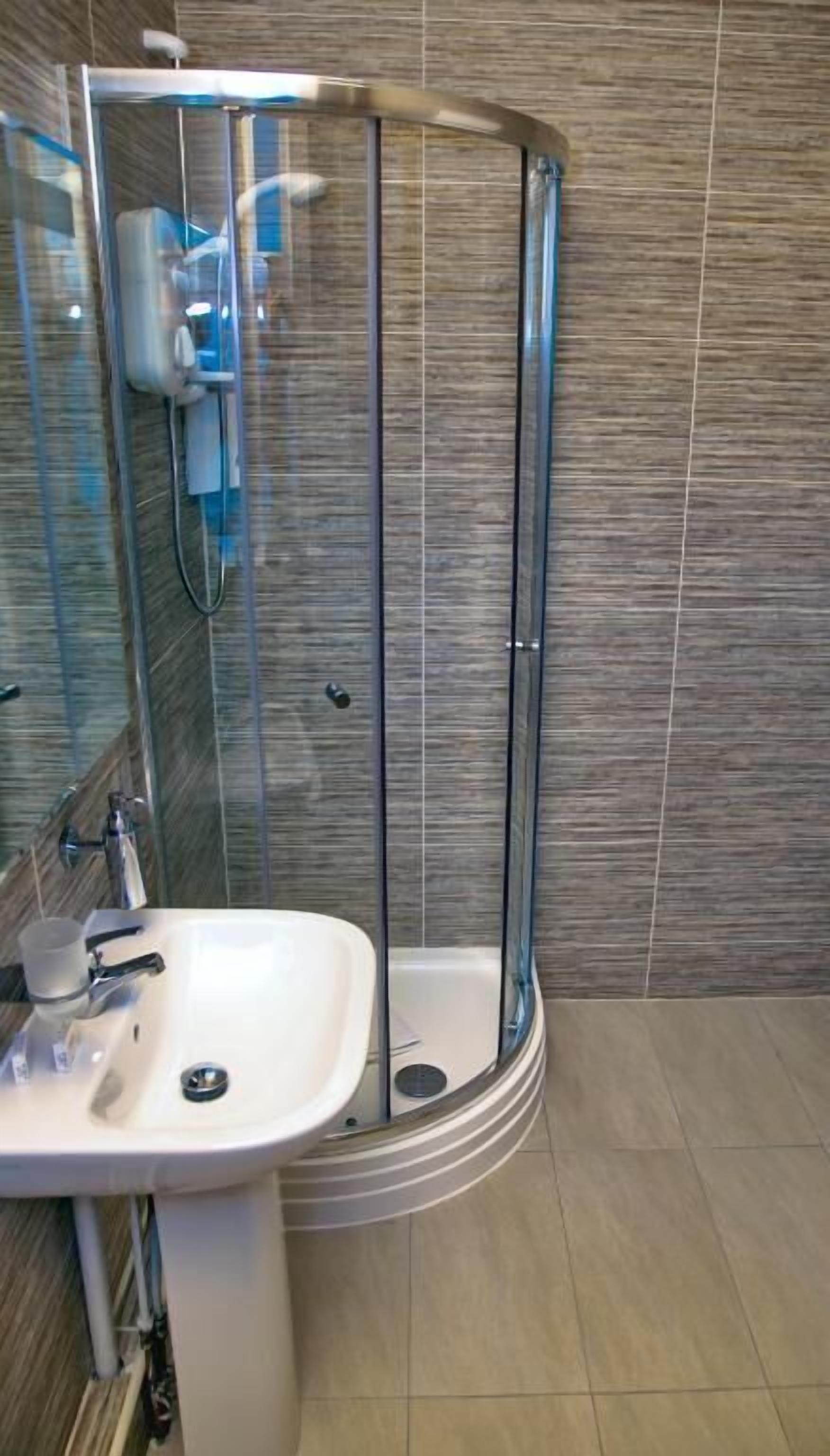 Ein modernes Badezimmer mit einer Duschkabine aus Glas, einem weißen Waschbecken und einem gefliesten Boden.