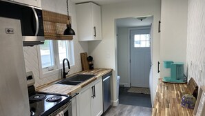 A modern kitchen with white cabinets, a black stove, a sink, and a coffee machine. - All Season Cottage steps to Long Beach (Wainfleet)