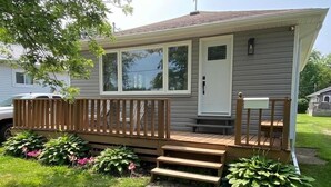 A single-story mobile home with a wooden deck, a front door, and a small porch area. - All Season Cottage steps to Long Beach (Wainfleet)