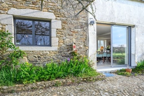 A stone building with a window and a door leading to an interior with a table and chairs.