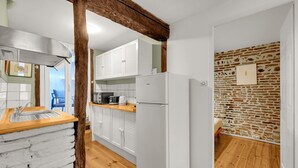 A compact kitchen with white cabinets, a wooden countertop, and a stone wall. - Hippolyte - Appt avec terrasse couverte (Toulouse)