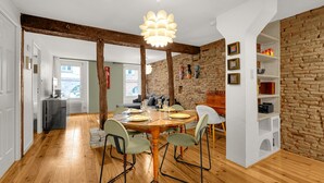 A dining area with a wooden table set for four, surrounded by green chairs. A modern pendant light hangs above the table. - Hippolyte - Appt avec terrasse couverte (Toulouse)