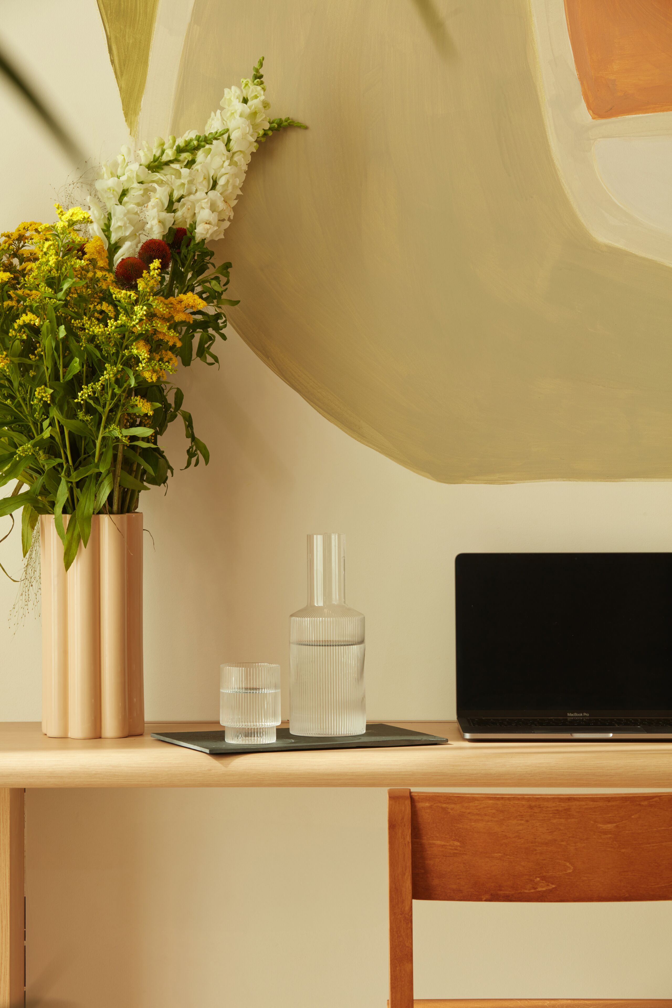 A desk with a laptop, a vase of flowers, and a water bottle.