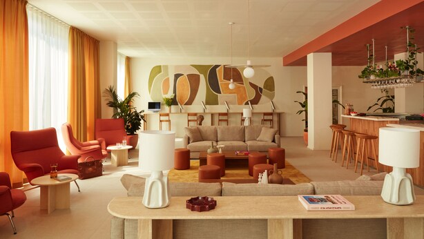 Ein modernes Wohnzimmer mit einer Sofagarnitur, roten Sesseln und einem Couchtisch. Es gibt eine Bar mit Hockern und einer Pflanze.