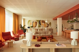 Una sala de estar moderna con un conjunto de sofás, sillones rojos y una mesa de centro. Cuenta con una zona de bar con taburetes y una planta.