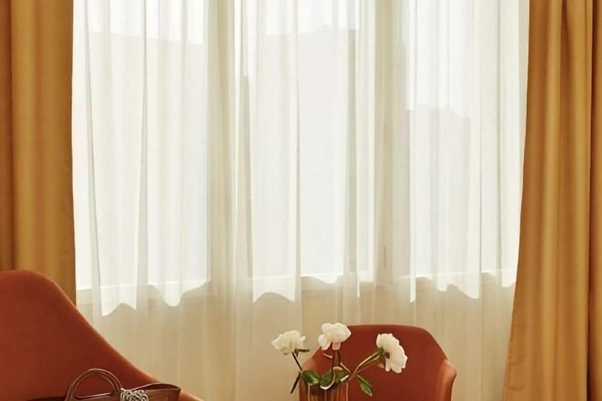 A room with a window, a chair, and a vase with flowers.