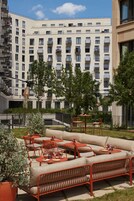 Un espacio al aire libre con mobiliario metálico rojo y vistas a un edificio de varios pisos con balcones.