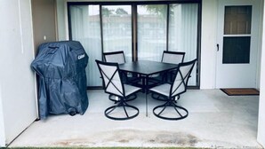 En overdækket terrasse med bord og stole, grill og en skydedør i glas.