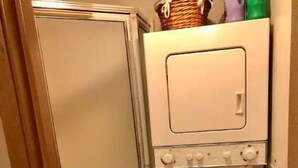 Ett kompakt tvättrum med tvättmaskin och torktumlare, en duschdörr och en liten korg placerad på torktumlaren.