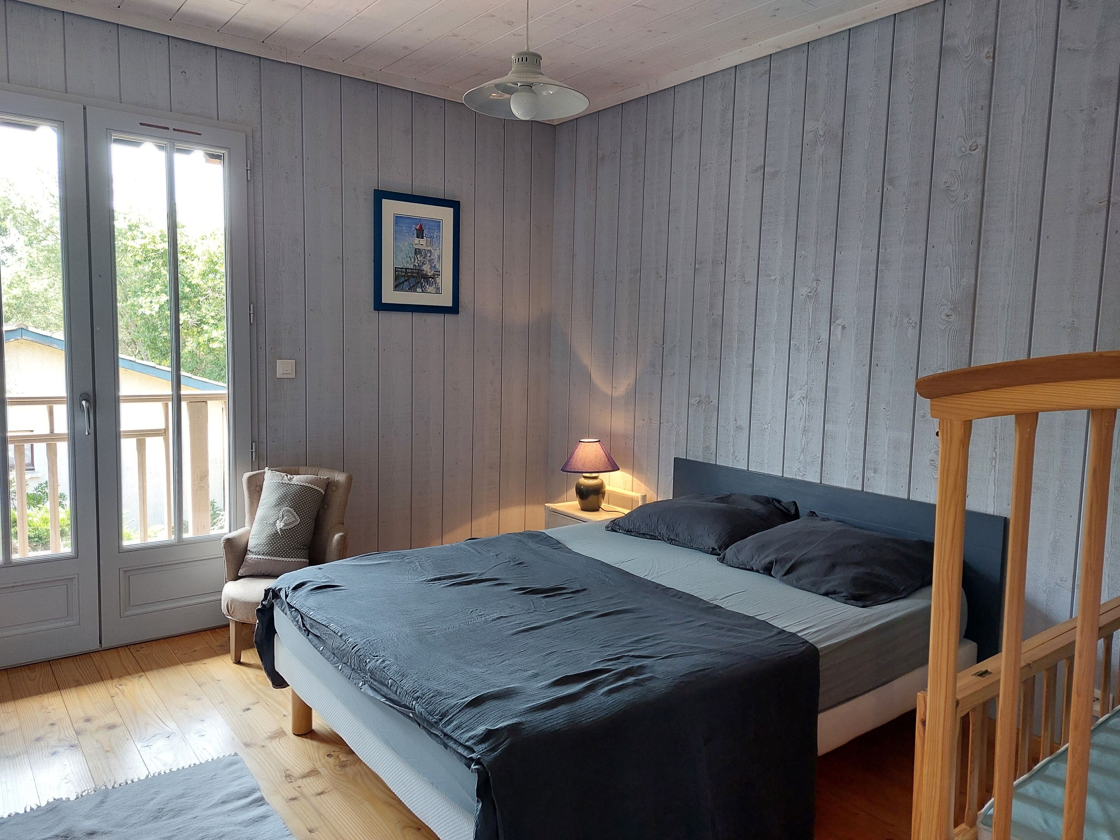 Un dormitorio con una cama, una silla, una mesita de noche con lámpara y un cuadro en la pared.