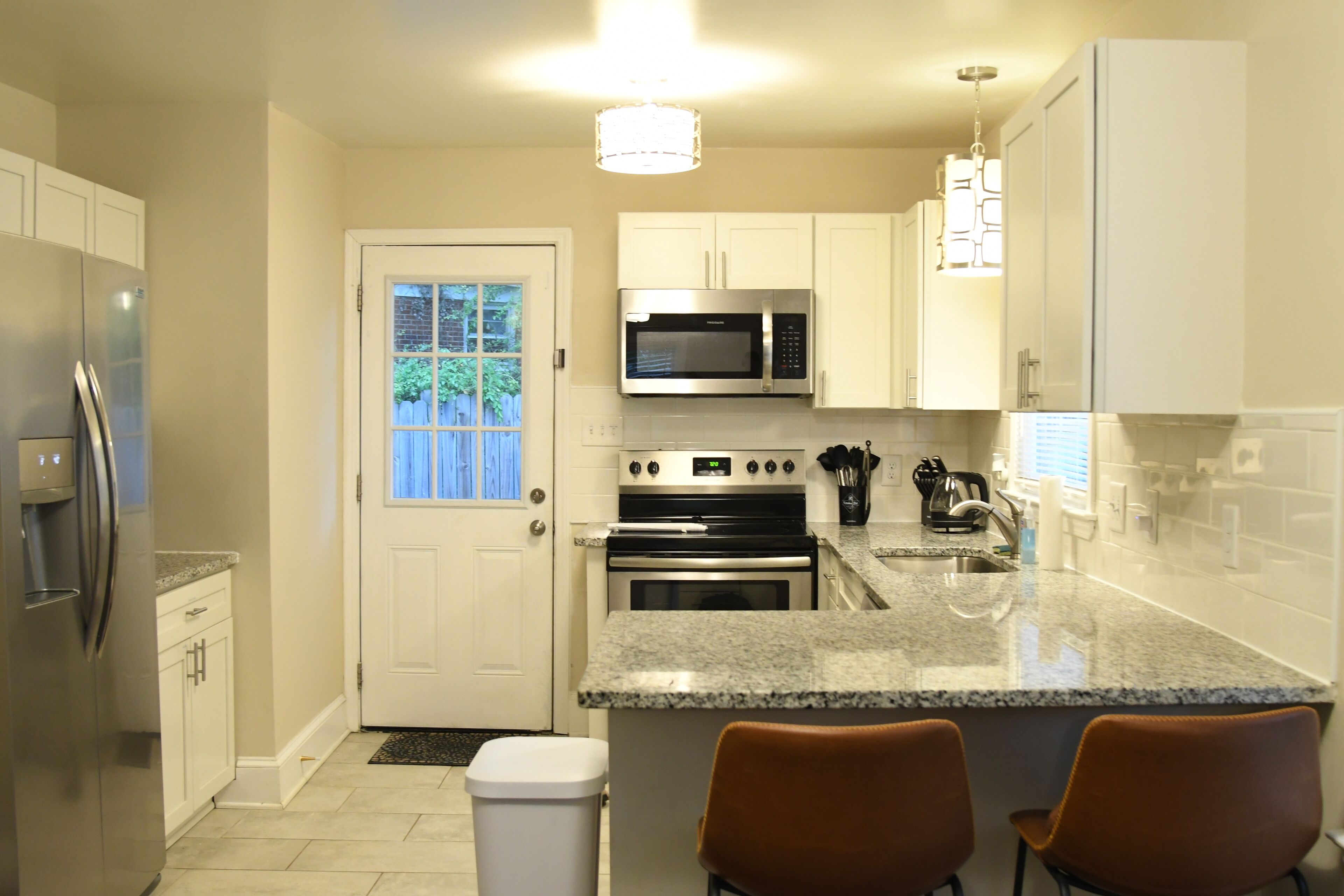 A modern kitchen with white cabinets, stainless steel appliances, granite countertops, and two brown bar stools.