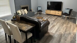 A modern living room with a fireplace, a large flat-screen TV, a dining area with a marble table, and a ceiling fan. - Modern 3BR 2BA West Enid (Enid)