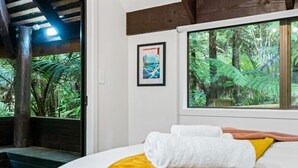 A room with a bed, a window with a view of a forest, and a framed picture on the wall.