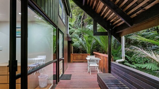 A wooden deck with a glass door leading to a room, surrounded by lush greenery.