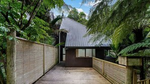 A wooden deck leading to a building with a metal roof, surrounded by lush greenery.