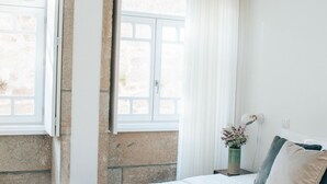 A bedroom with a bed, a window with curtains, a vase with flowers, and a nightstand.