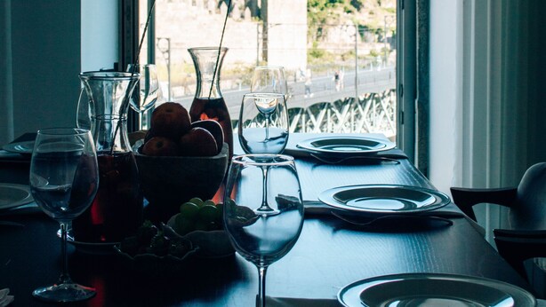 A dining table set with wine glasses, plates, and a pitcher, with a view of a historic building and greenery outside.