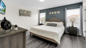 Une chambre à coucher comprenant un lit, des tables de chevet, un bureau, une plante en pot et des œuvres d’art accrochées aux murs.