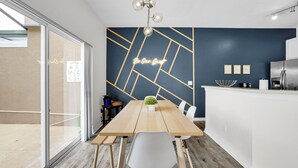 Une cuisine moderne avec une table en bois, des chaises blanches et un néon mural.