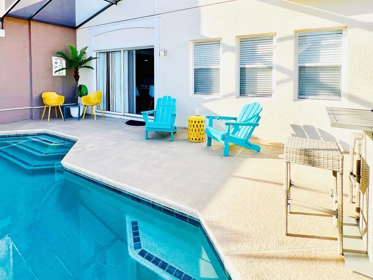 Una piscina con una línea de agua azul cristalina, rodeada por una plataforma de concreto. Hay dos sillas Adirondack turquesa y una silla amarilla cerca de la piscina.