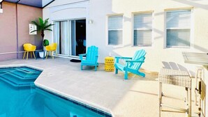 Une piscine à l’eau d’un bleu limpide, bordée d’une terrasse en béton. On y trouve deux fauteuils Adirondack turquoise et une chaise jaune près de la piscine.