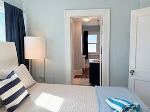 A hotel room with a bed, a bedside lamp, a window with curtains, and a view into the bathroom.