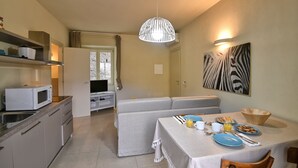 Cocina compacta con microondas, una mesa de comedor dispuesta con platos, tazas y un cuenco. Se ve un sofá al fondo y una obra de arte con estampado de cebra en la pared.
