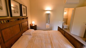 Una cama bien hecha con cabecera de madera, una lámpara de noche y cuadros en la pared.