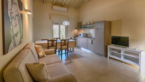 A living room with a sofa, a dining table, chairs, a TV on a stand, and a kitchen area with cabinets and a microwave. - Appartamento Billy by Theater Home - with partial lake view and garage (Tignale)
