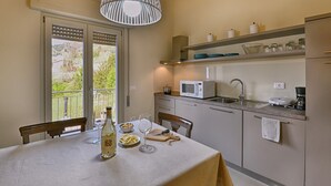 A kitchen with a dining table, a hanging light fixture, a window with a view, and a microwave. - Appartamento Billy by Theater Home - with partial lake view and garage (Tignale)