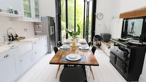 Una cocina moderna con armarios blancos, una mesa de comedor de madera para cuatro personas y un ventanal con vistas a la vegetación.