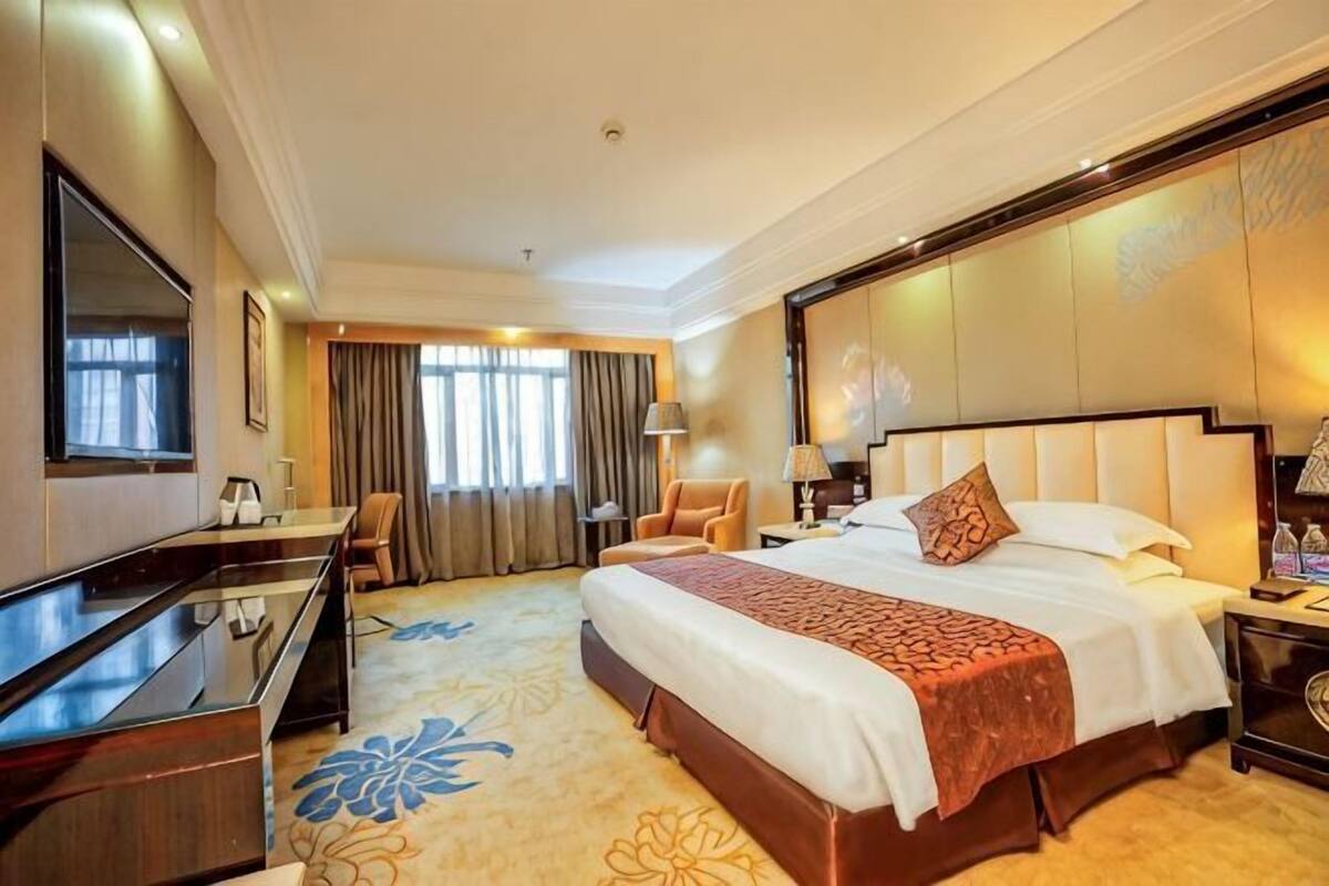 A hotel room with a large bed, a desk, a TV, and a view of the outdoors.