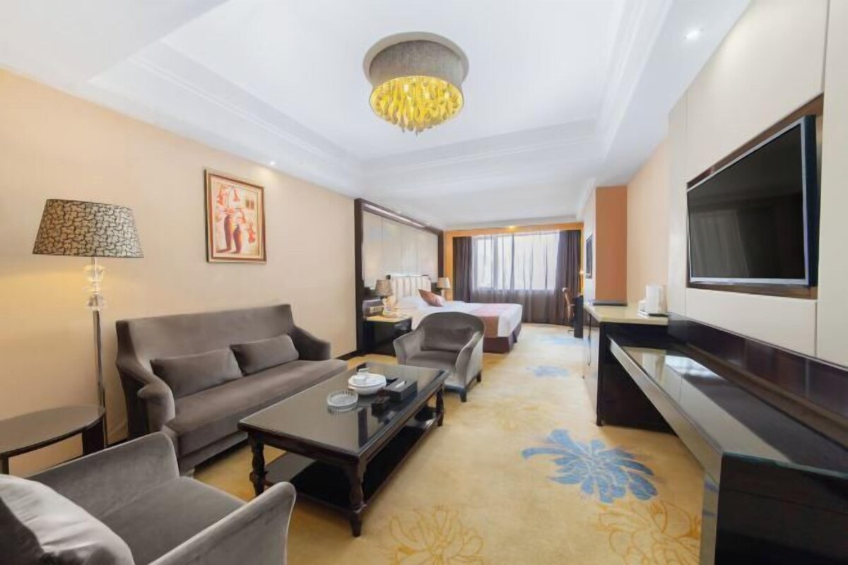 A hotel room with a sofa, armchairs, a coffee table, a TV, a desk, and a bed.