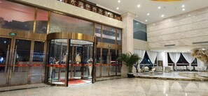 A hotel lobby with a revolving door entrance, a reception desk, and a seating area with a large window. - Weihua Internationai Hotel (Hui'an)
