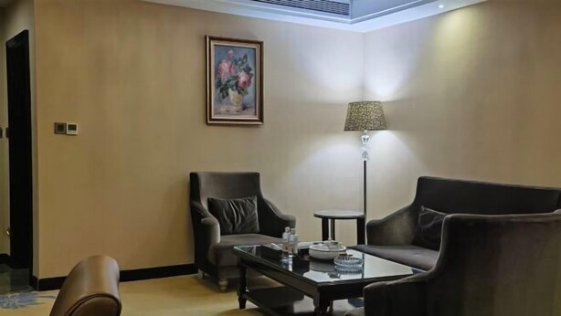 A hotel room with a sofa, armchair, coffee table, lamp, and a painting on the wall. - Weihua Internationai Hotel (Hui'an)