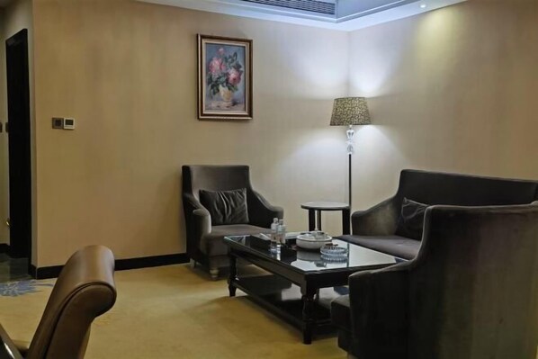 A hotel room with a sofa, armchair, coffee table, lamp, and a painting on the wall. - Weihua Internationai Hotel (Hui'an)