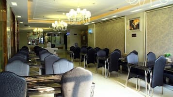 A hotel dining area with multiple tables and chairs, chandeliers, and a mirror reflecting the space.
