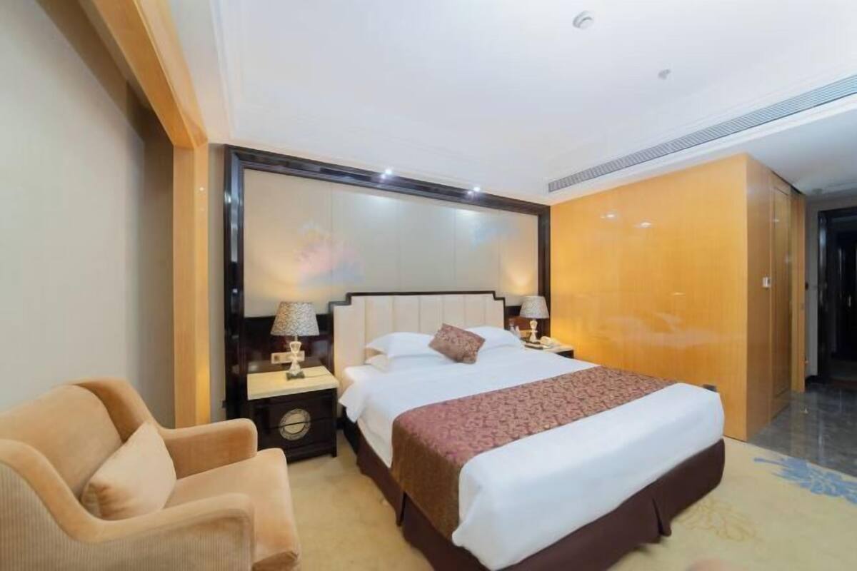 A hotel room with a large bed, bedside tables, a chair, and a wardrobe.
