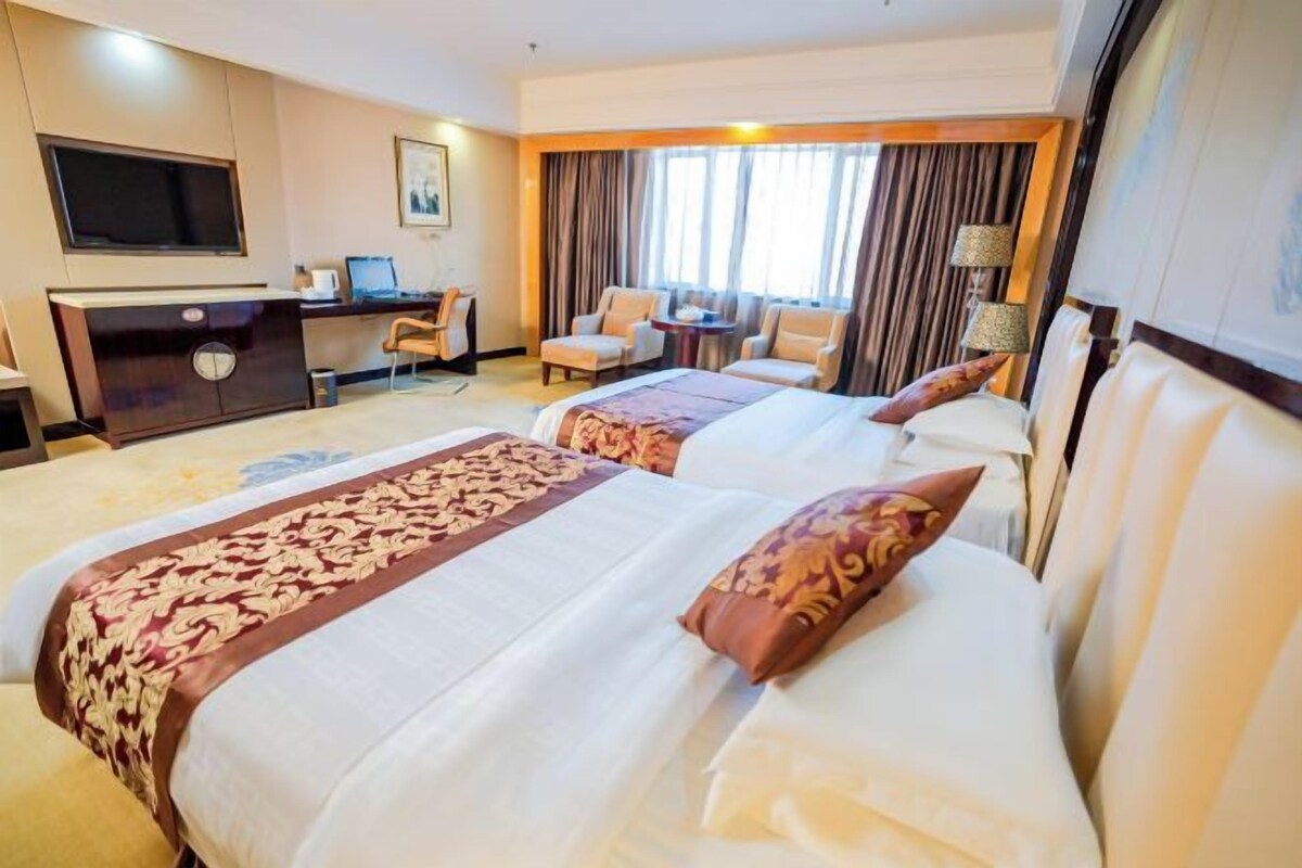 A hotel room with two beds, a desk with a computer, a TV, and a seating area with chairs.
