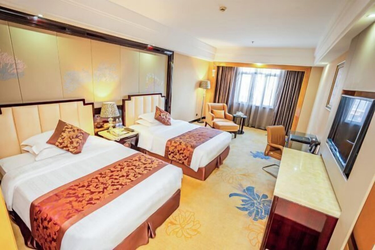 A hotel room with two beds, a desk, a chair, a TV, and a large window with curtains.