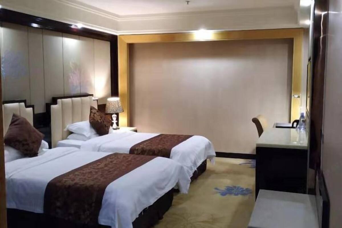 A hotel room with two beds, a desk, a chair, and a large mirror.