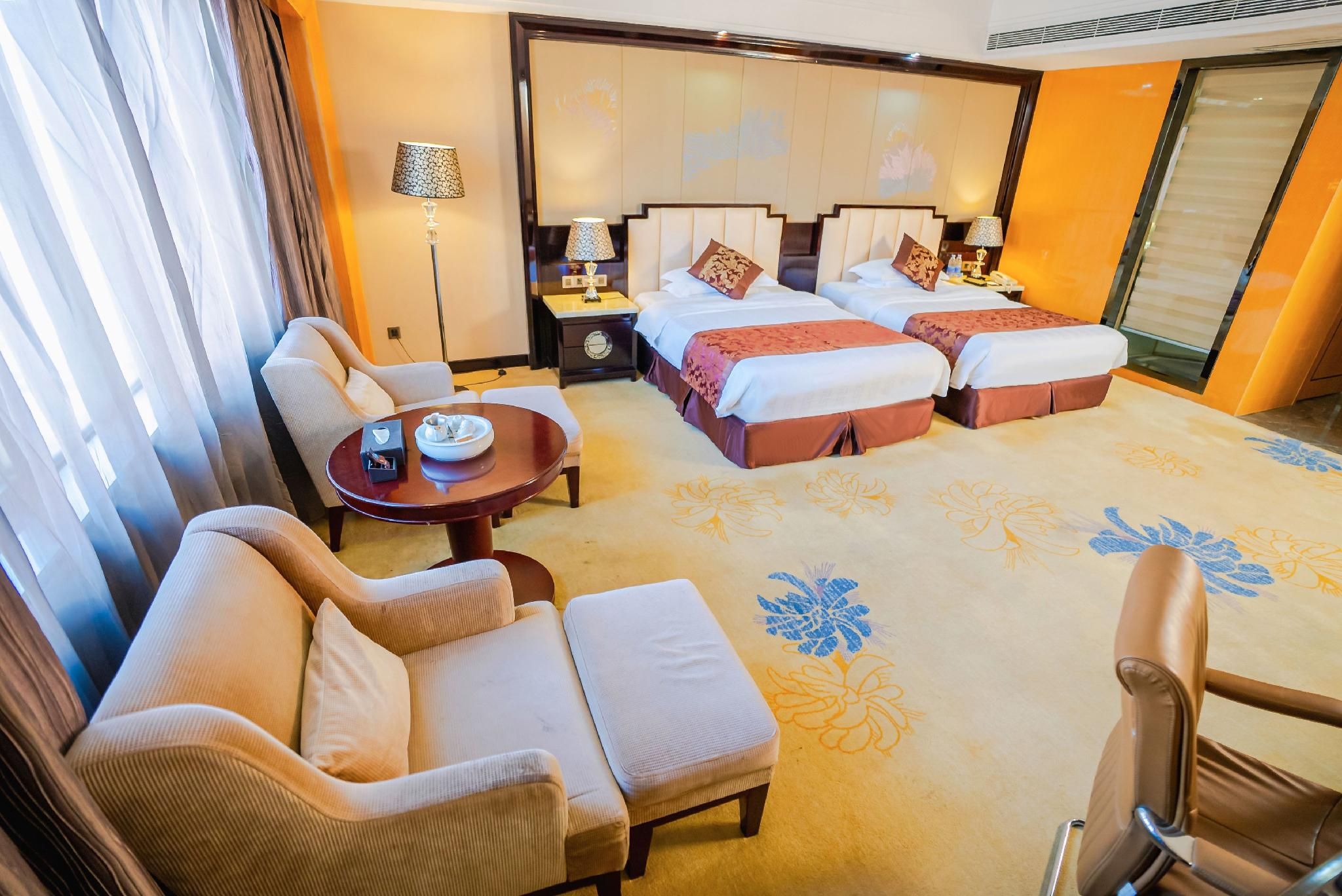 A hotel room with a sofa, a small table, a bed with two pillows, and a nightstand with a lamp.
