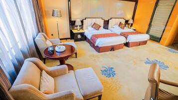 A hotel room with a sofa, a small table, a bed with two pillows, and a nightstand with a lamp.