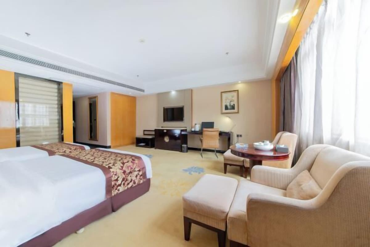 A hotel room with a large bed, a desk, a chair, and a sofa.